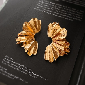 Détail macro de boucles d'oreilles dorées en éventail avec texture plissée sur livre d'art