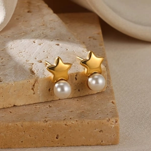 Detail view of gold starfish stud earrings with white pearl drop on beige stone
