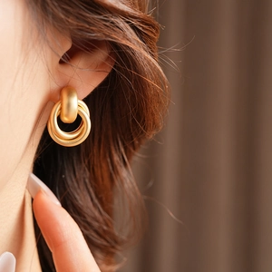 Close-up of matte gold geometric interlocking hoop earrings worn by a model