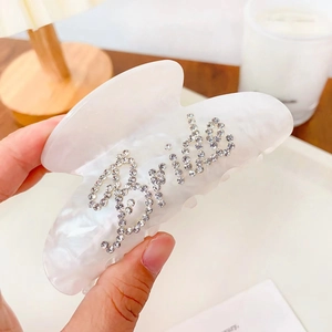 Close-up of cream acetate hair claw with rhinestone lettering on a marble texture surface