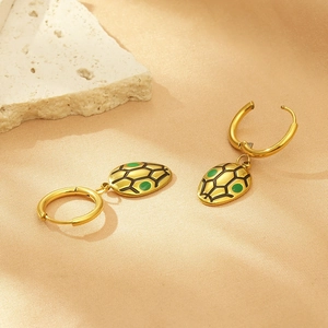 Detailed shot of golden tortoise shell earrings with green accents on a textured stone