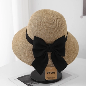 Detail of woven straw sun hat featuring a black ribbon bow and UV protection hangtag