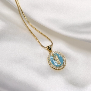 Macro shot of gold Mary pendant with blue enamel and clear crystals on white silk