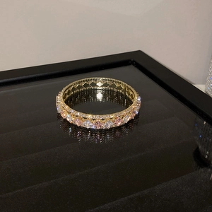 Detailed close-up of golden bangle with pink and white zircon stones on black mirror