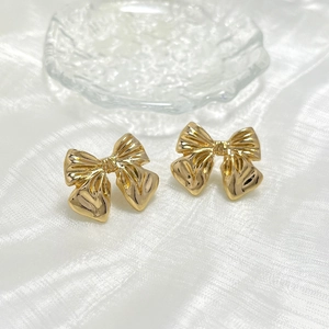 Detailed view of elegant gold bow stud earrings with polished metallic surface on white silk