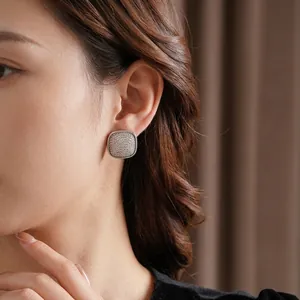 Square silver stud earrings with pavé diamonds on a model with soft shadows