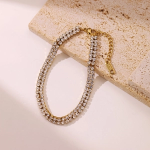 Double-row cubic zirconia gold-plated stainless steel bracelet on beige stone display