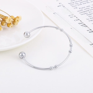 Detail of minimalist stainless steel open bangle with sliding beads on a white surface