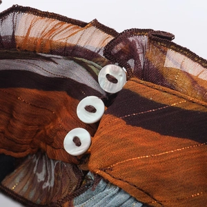 Macro view of asymmetrical printed top with pearl buttons and ruffled edges