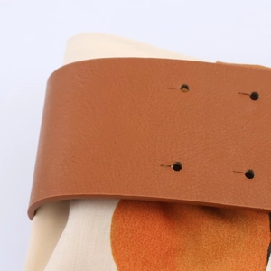 Detailopname van de bruine leren riem en oranje bedrukte popeline stof op de rok