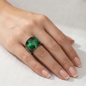 Detailed close-up of emerald green faceted crystal ring on a model with silver band