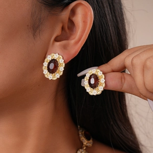 Close-up of vintage gold floral earrings with a deep red oval gemstone on a model