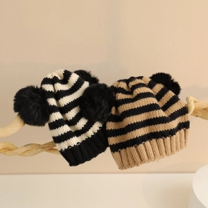 Dettaglio del berretto in maglia a righe per neonati con pompon su decoro in legno