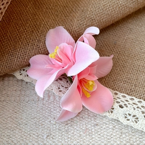 Close-up of a delicate pink fabric flower hairpin with yellow stamens on rustic burlap.
