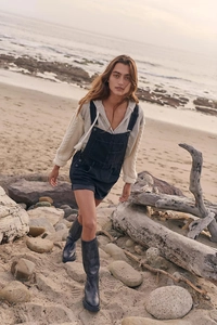 Outdoor shot of black denim overalls paired with a knit hoodie and black tall boots