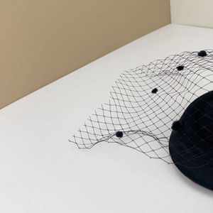 Detail of vintage black fascinator hat with mesh veil and small pom pom decorations