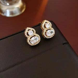 Detailed view of gold gourd earrings with oval gemstones on a luxury brown leather case