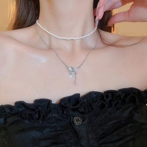 Detail of layered necklace featuring white pearls and a silver butterfly pendant with blue zircon