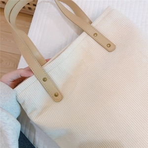Detail of corduroy tote bag featuring ivory fabric texture and tan faux leather handles