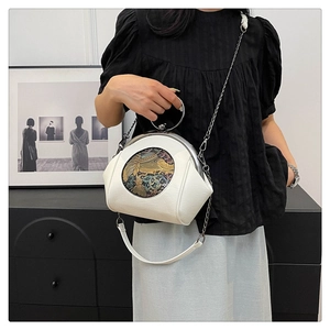 Detail of cream shell bag with metal ring handle and artistic embroidered centerpiece