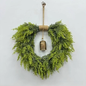 Christmas heart wreath with green cedar leaves and vintage brass bell on rustic rope