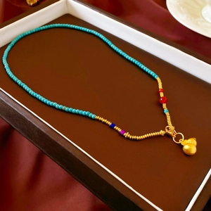 Détail du collier de perles vertes avec pendentif gourde dorée dans un coffret à bijoux