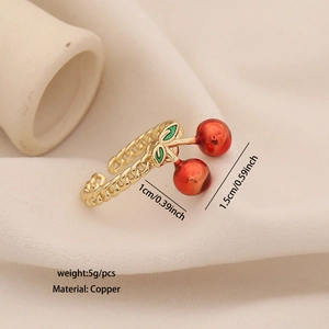 Minimalist gold open ring with red cherry and green leaf design on fabric