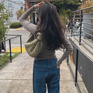 Rear view of a model wearing a slim-fit ribbed long sleeve top with a woven leather handbag
