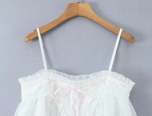 Detailaufnahme von weißem Spitzentop mit rosa Bandschleifen und besticktem Netzgewebe