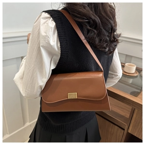 Close-up of a brown leather shoulder bag with gold hardware worn by a model