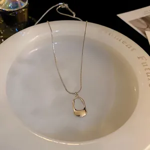 Minimalist stainless steel necklace with geometric pendant on a white ceramic dish