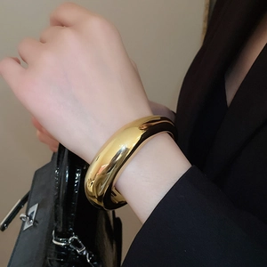 Bracelet jonc doré poli avec motif rayé ovale porté par un mannequin en noir
