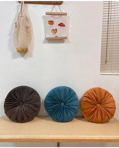 Three plush velvet pumpkin cushions in brown, teal, and orange on a rattan bench