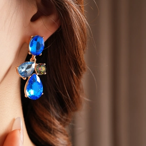 Close-up of vintage gold teardrop earrings with blue and multicolor gemstones on a model