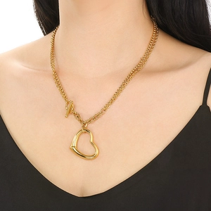 Gros plan d'un collier doré double épaisseur avec pendentif cœur ajouré et fermoir en T