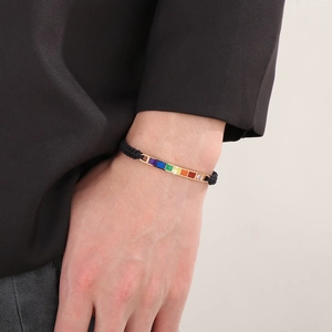 Rainbow enamel charm on black braided cord bracelet shown on a wrist with black suit