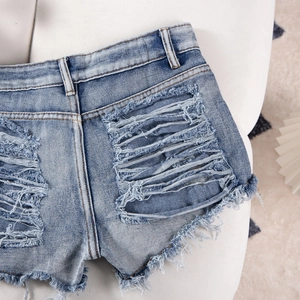 Detailed view of blue denim shorts with heavy distressing and frayed edges on fabric