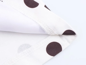 Vue détaillée des coutures overlock et du motif à pois noirs sur tissu blanc