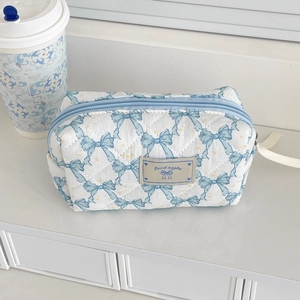 Close-up of quilted bow cosmetic bag featuring blue metal zipper and ribbon patterns