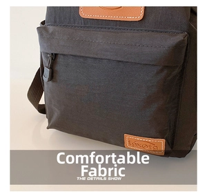 Detail of black nylon backpack featuring a zip pocket and leather brand patch on the surface