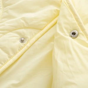Close-up of diamond quilted fabric with silver metal snap buttons on a pale yellow jacket