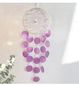 Detail of dream catcher featuring purple shell discs and moon pendant in soft light