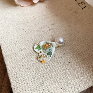Détail d'une pince à cheveux avec fleurs 3D, feuilles vertes et une grande perle blanche