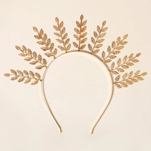 Detail of golden metal headband featuring seven symmetrical leaf motifs on beige backdrop