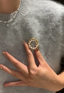 Close-up of 24k gold-plated round brooch with shiny pearls and zircons on grey sweater