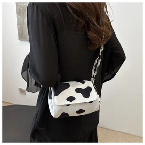 Detailed back view of a cow print crossbody bag worn with a black chiffon top