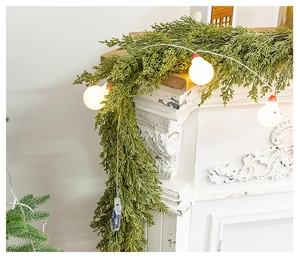 Close-up of artificial cedar garland with snowman LED lights on a white fireplace