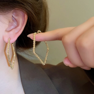 Close-up of golden irregular geometric hoop earrings featuring hammer texture on model