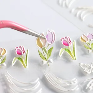 Macro shot of 5D embossed tulip nail stickers being applied with tweezers on white background