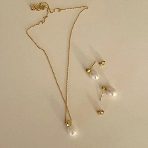Elegant gold necklace and pearl earrings set displayed on a minimalist beige background